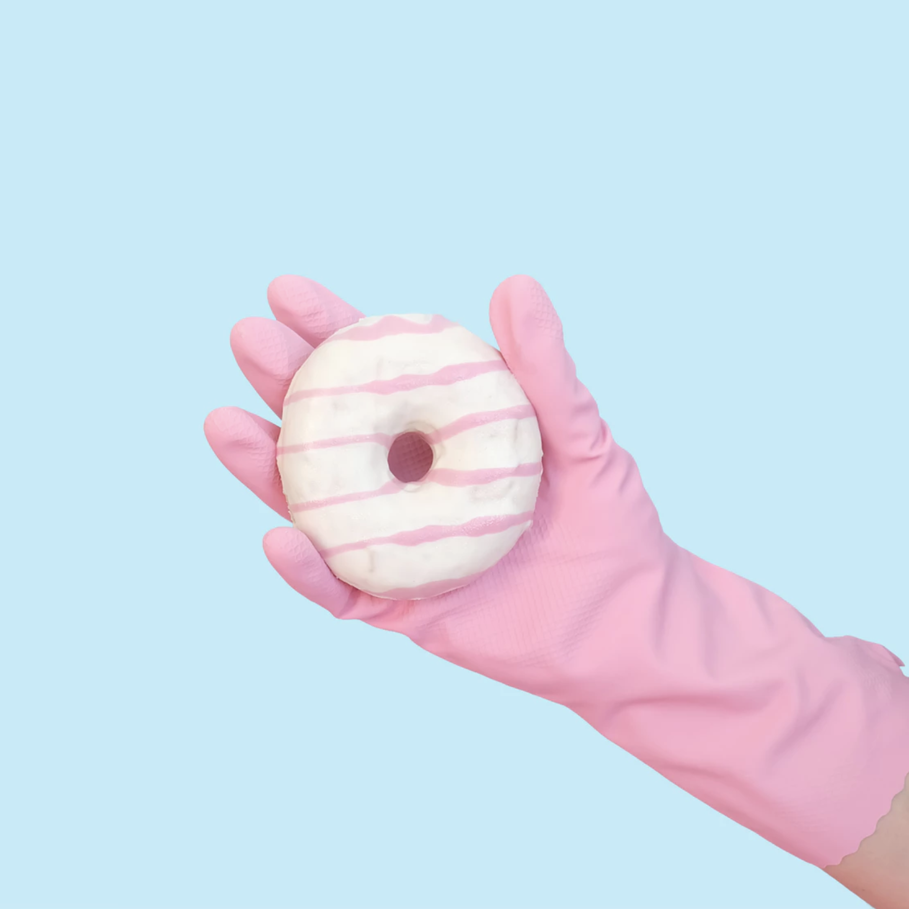 pink gloved hand holding a pink and white glazed doughnut